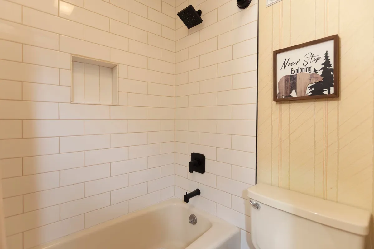 A serene, modern bathroom highlighted by crisp white subway tiles, black fixtures, and a stylish bathtub. Decorative wall art and neatly arranged accessories complete the look, making the space feel inviting for both soothing baths and quick showers.
