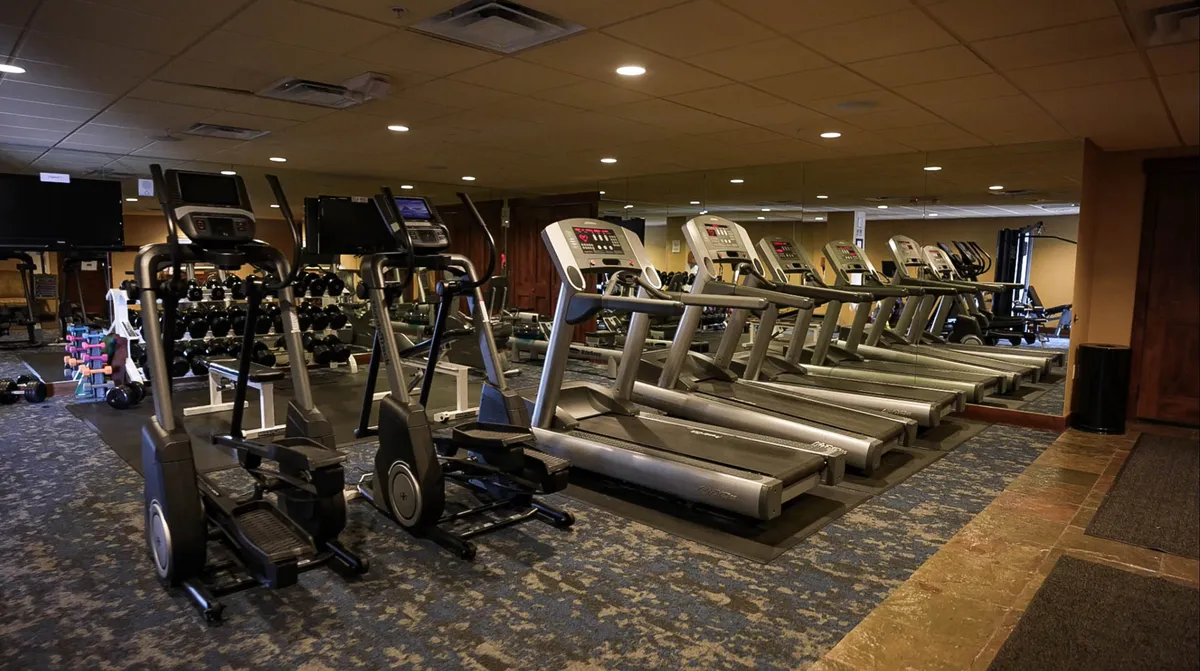 A bright, modern fitness center featuring treadmills, ellipticals, and a well-stocked dumbbell rack. The space is energetic, inviting guests to pursue their fitness routines, whether solo or in group classes. Natural light fills the room, adding to the motivating atmosphere.